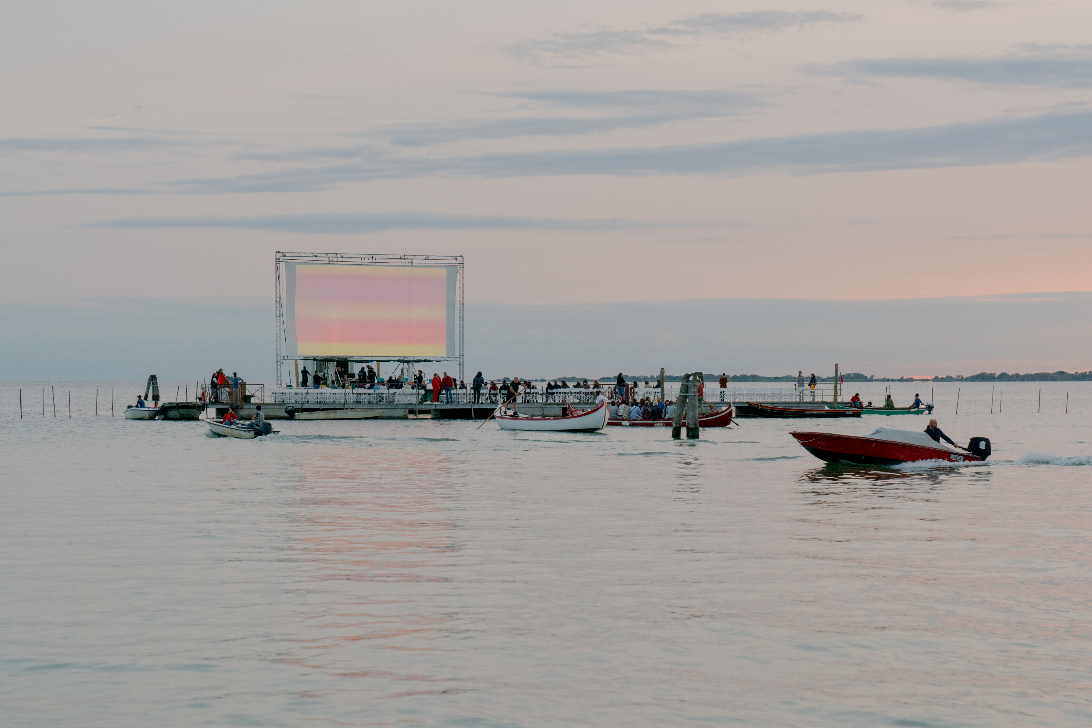 Schermo cinematografico allestito sulle acque di una laguna e contornato di barche