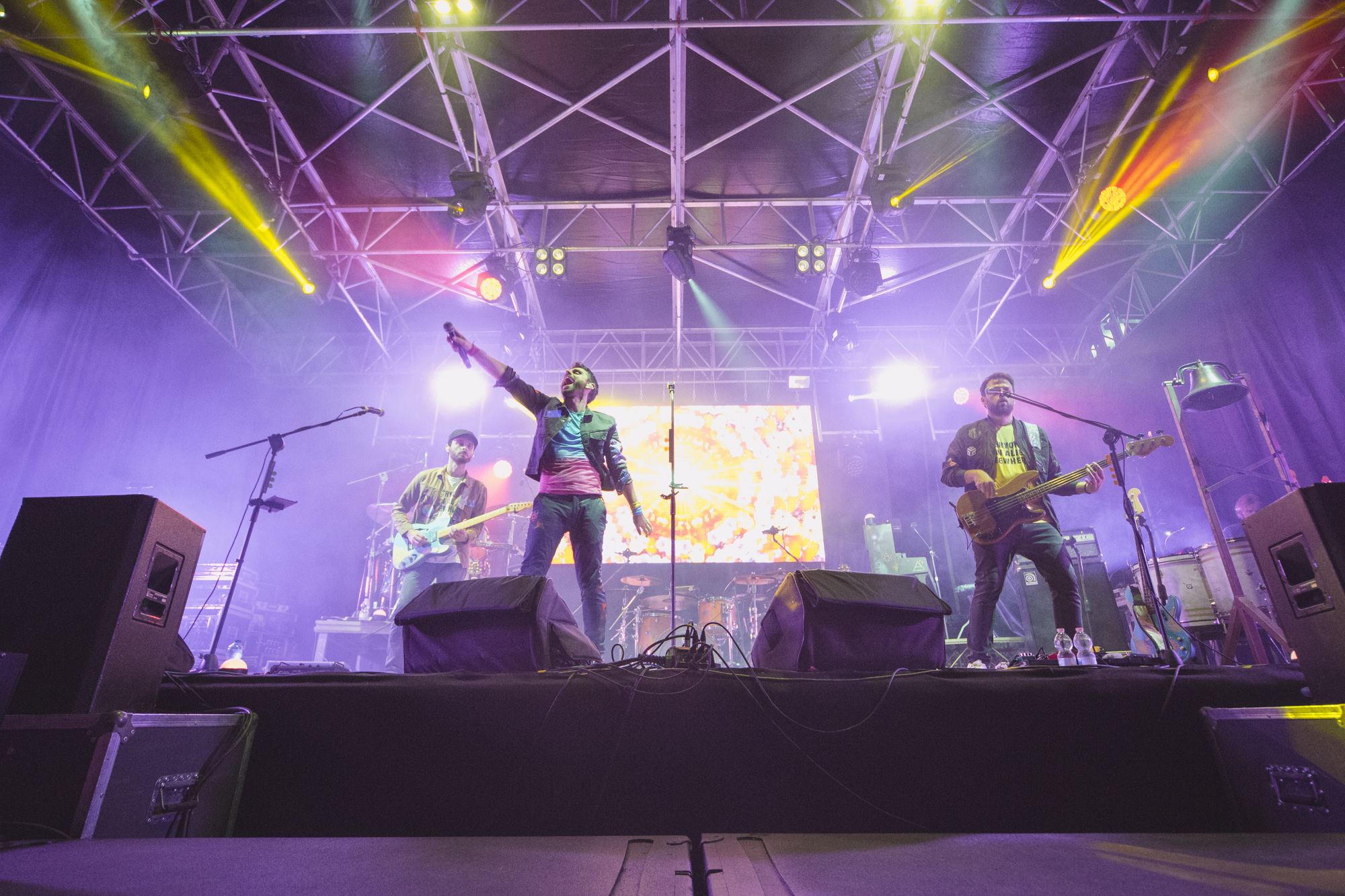 Tre musicisti di una band rock sul palco. Il cantante tende il microfono verso il pubblico