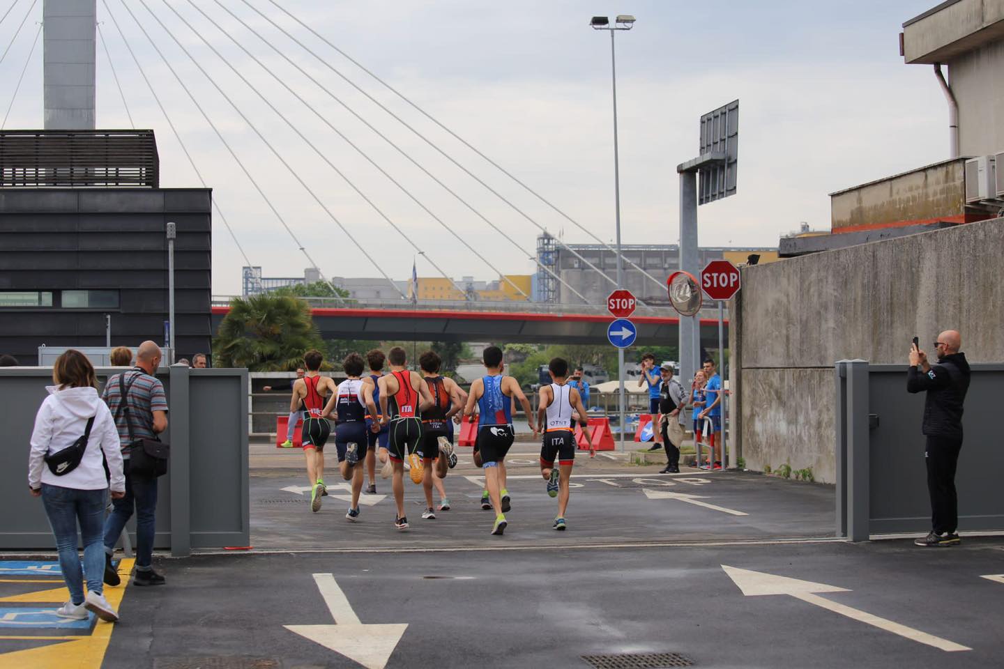 Gruppo di corridori visti spalle varca un cancello ed entra in un piazzale