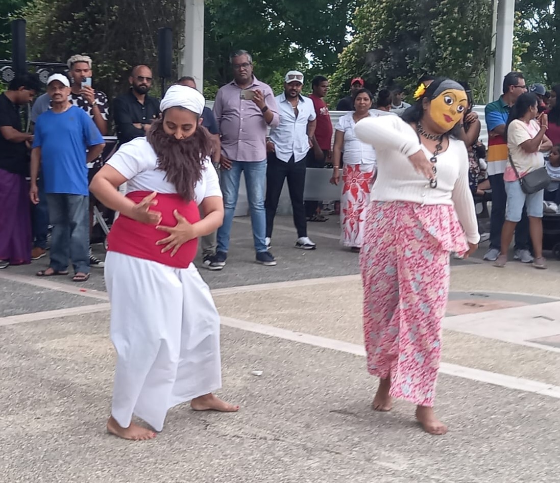 Due donne in abiti e maschere tradizionali singalesi ballano su un piazzale, attorniate da pubblico di persone dello Sri Lanka