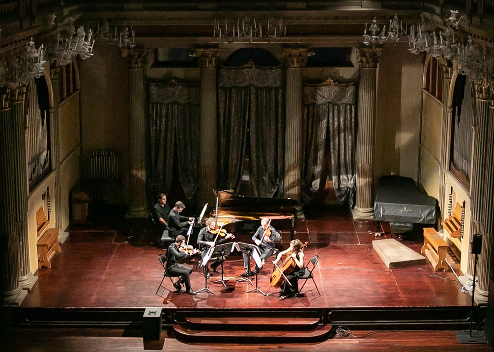 Su un palco suonano cinque musicisti: quattro agli archi e uno al pianoforte