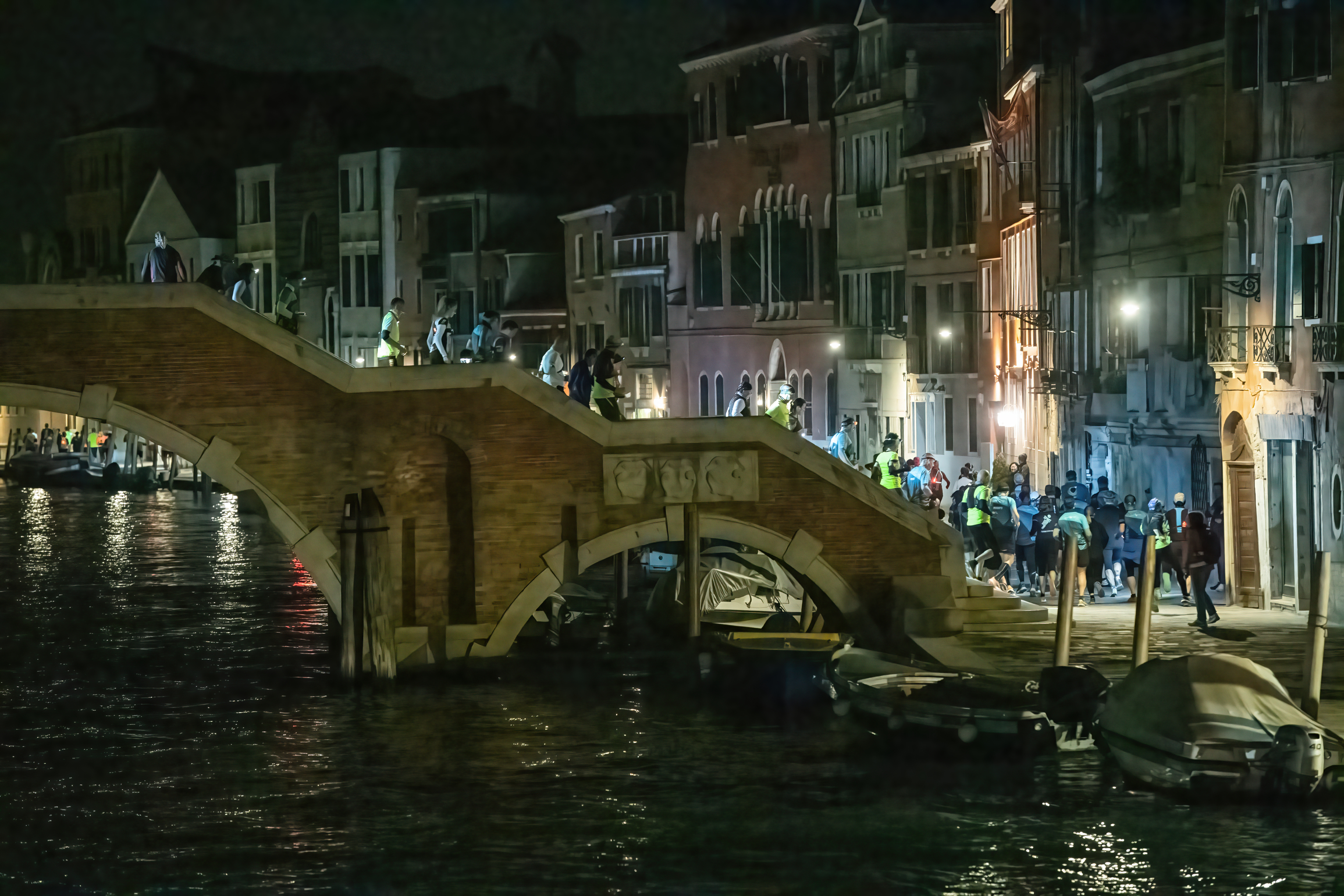 Gruppo di podisti con lampada sulla fronte discende un ponte di Venezia durante una corsa in notturna