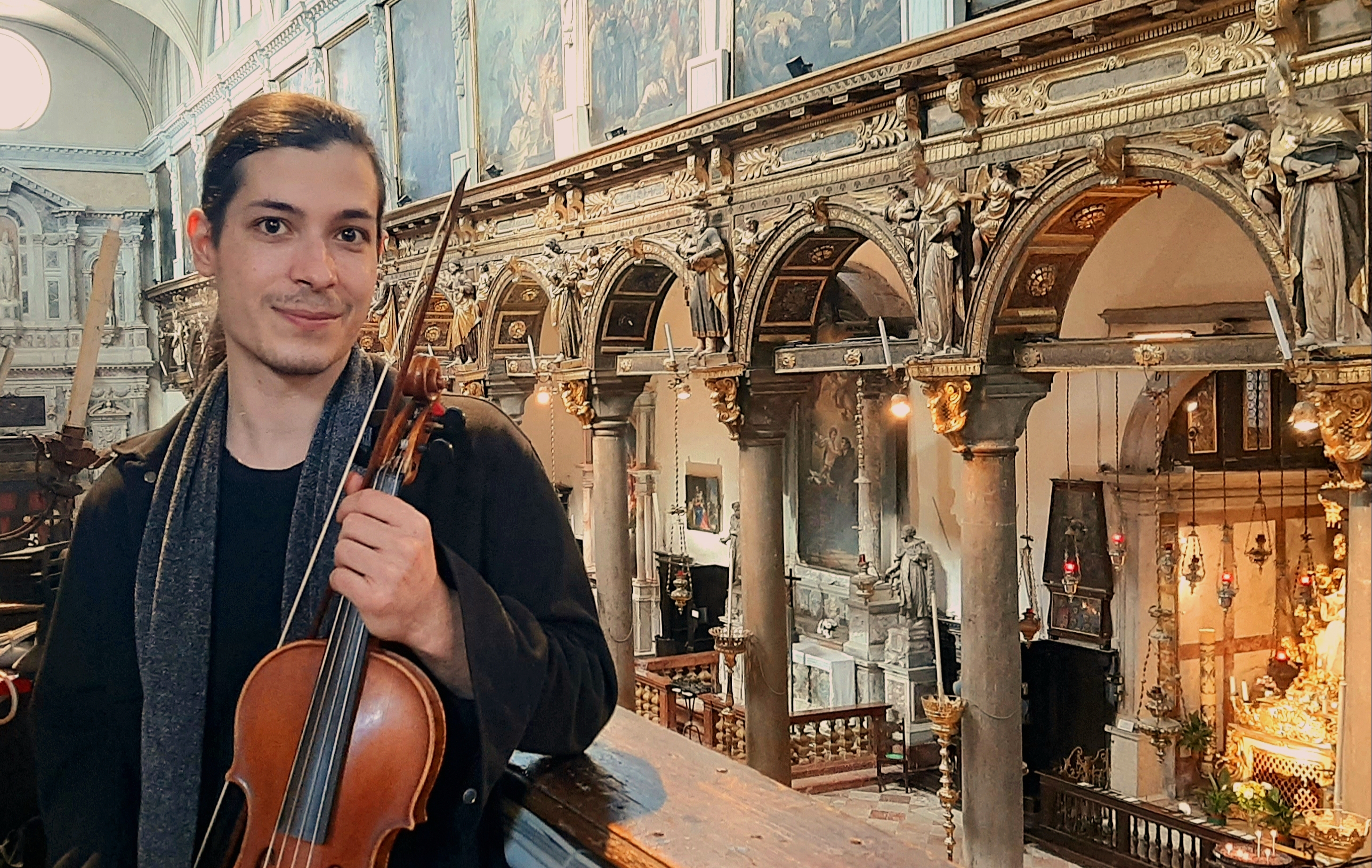 Sulla sx primo piano di giovane che tiene in mano un violino; sullo sfondo, l'interno di una chiesa