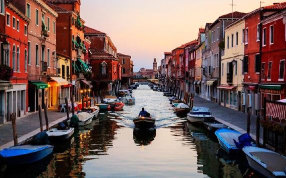 Vista di un canale veneziano dove sta navigando una barchetta pilotata da un uomo