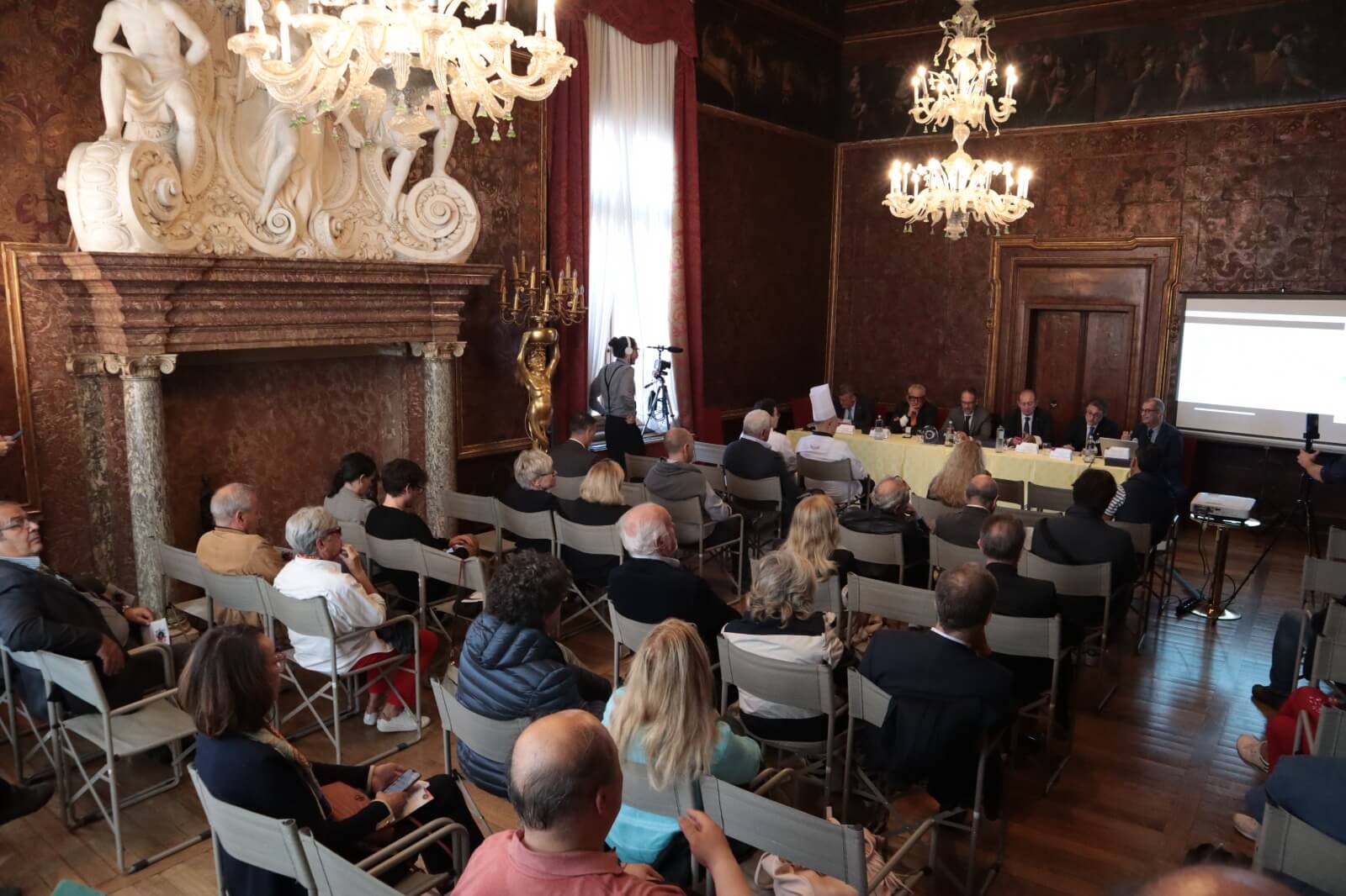 Pubblico seduto ascolta cinque conferenzieri al tavolo