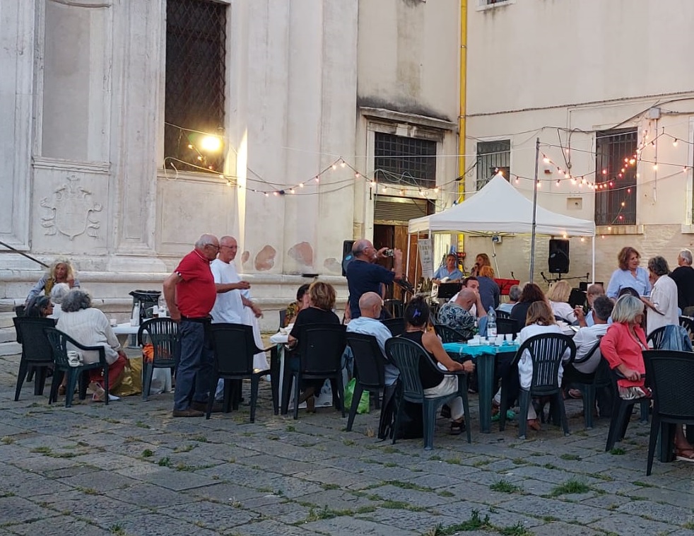 Gruppo di persone sedute a tavoli all'aperto, intente in una cena 