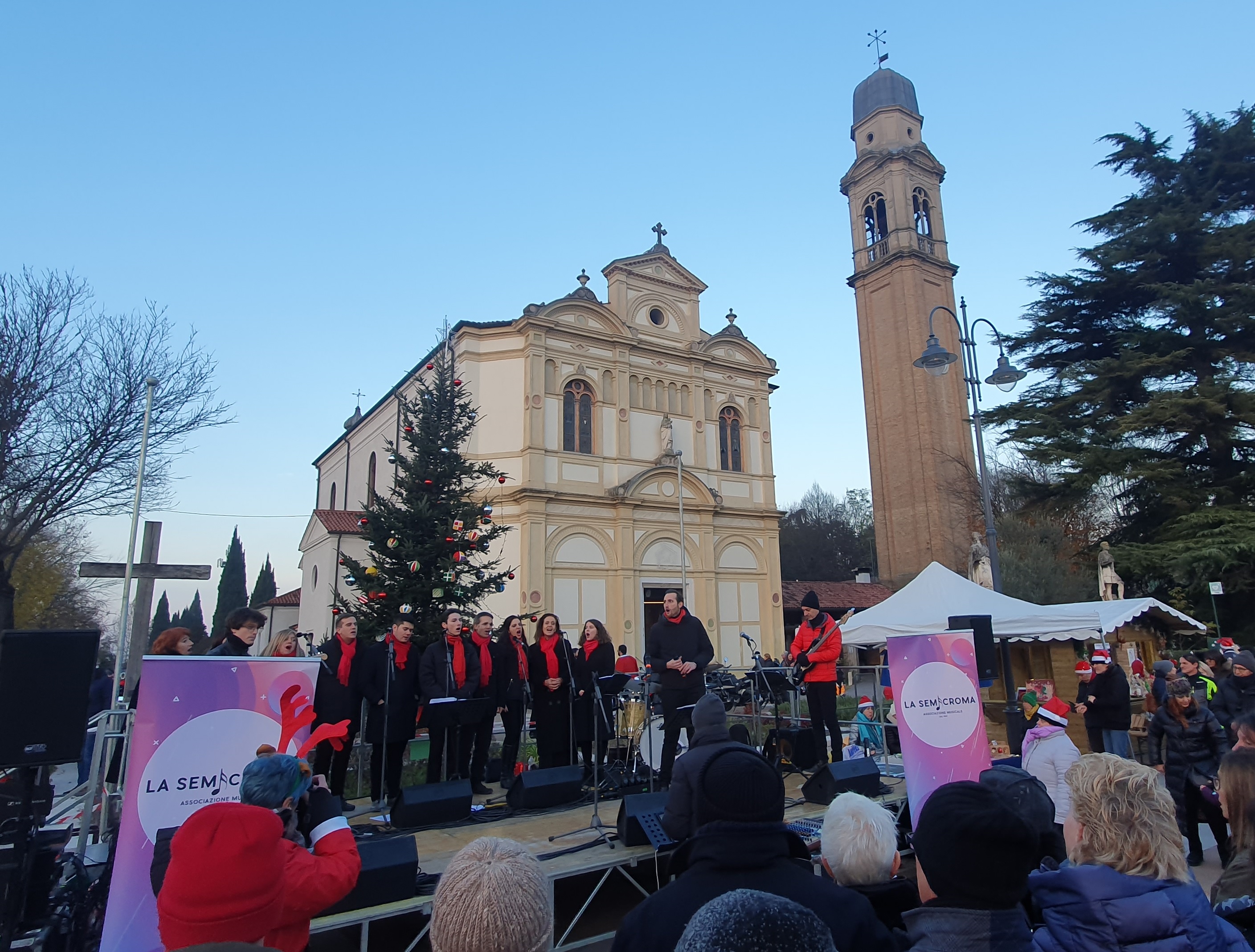 Coro canta su un palco all'aperto di fronte a una chiesa e davanti a un gruppo di persone