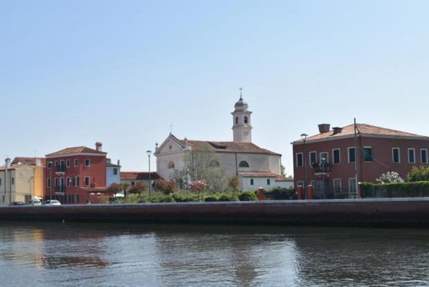 Veduta di uno scorcio di Pellestrina. In primo piano la laguna; dietro, una chiesa con campanile tra alcuni caseggiati