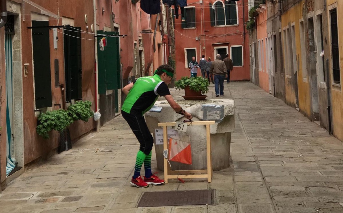 Atleta di una gara di orienteering a un punto di controllo posto su un pozzo in una calle veneziana