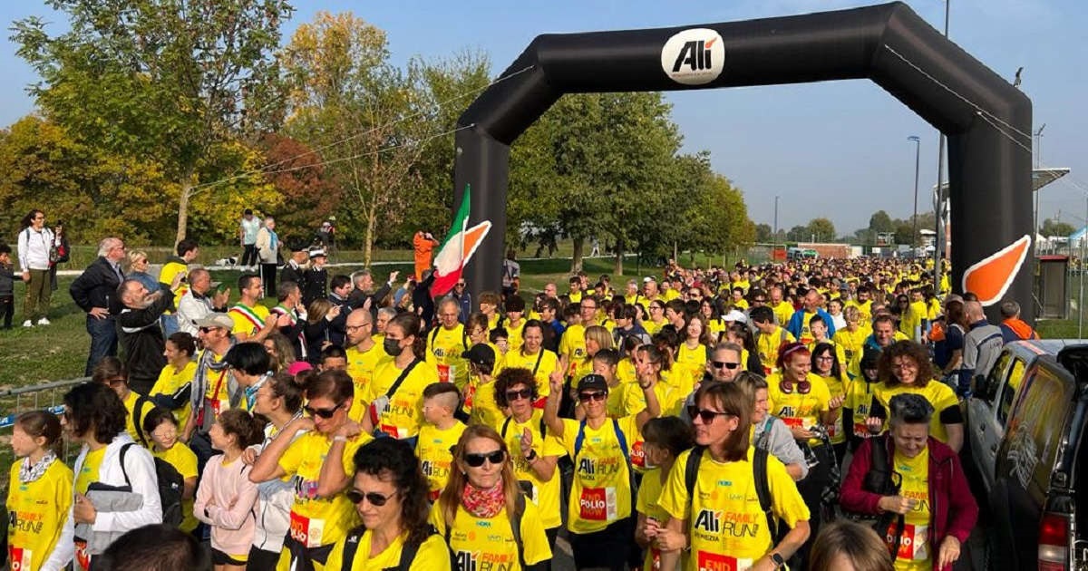 Partenza di una gara podistica: decine di adulti e bambini sfilano accalcati sotto un arco gonfiabile