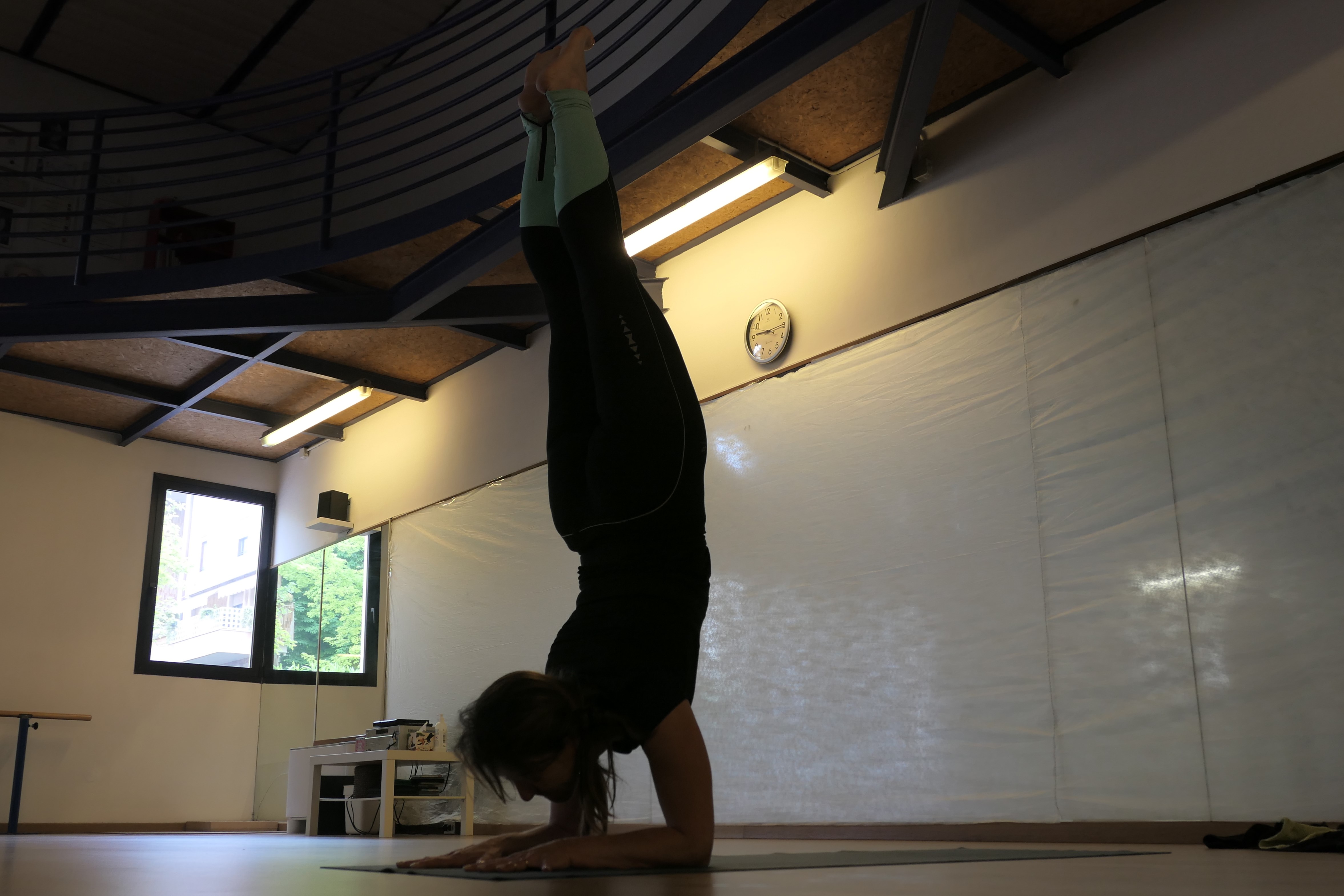 Donna fa esercizio pincha dello yoga (a testa in giù, gambe in alto a candela, avambracci appoggiati sul pavimento)