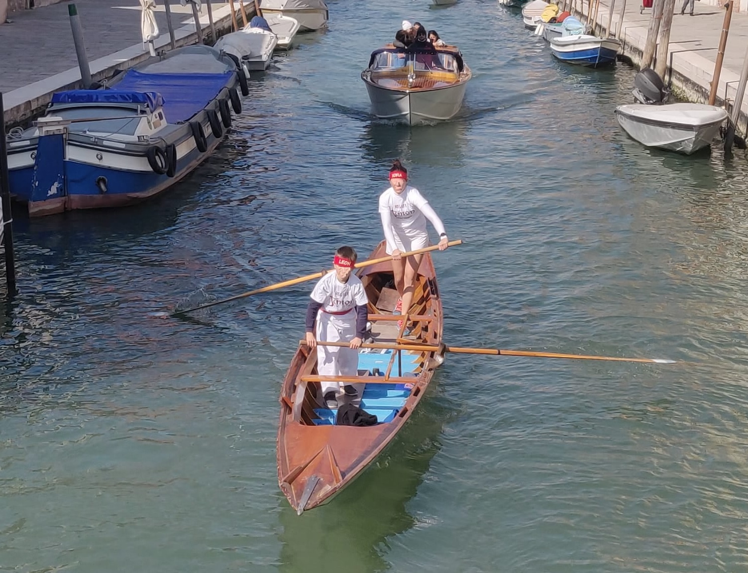 Un canale veneziani: in primo piano barca su cui vogano due ragazzi, dietro, invece, un motoscafo